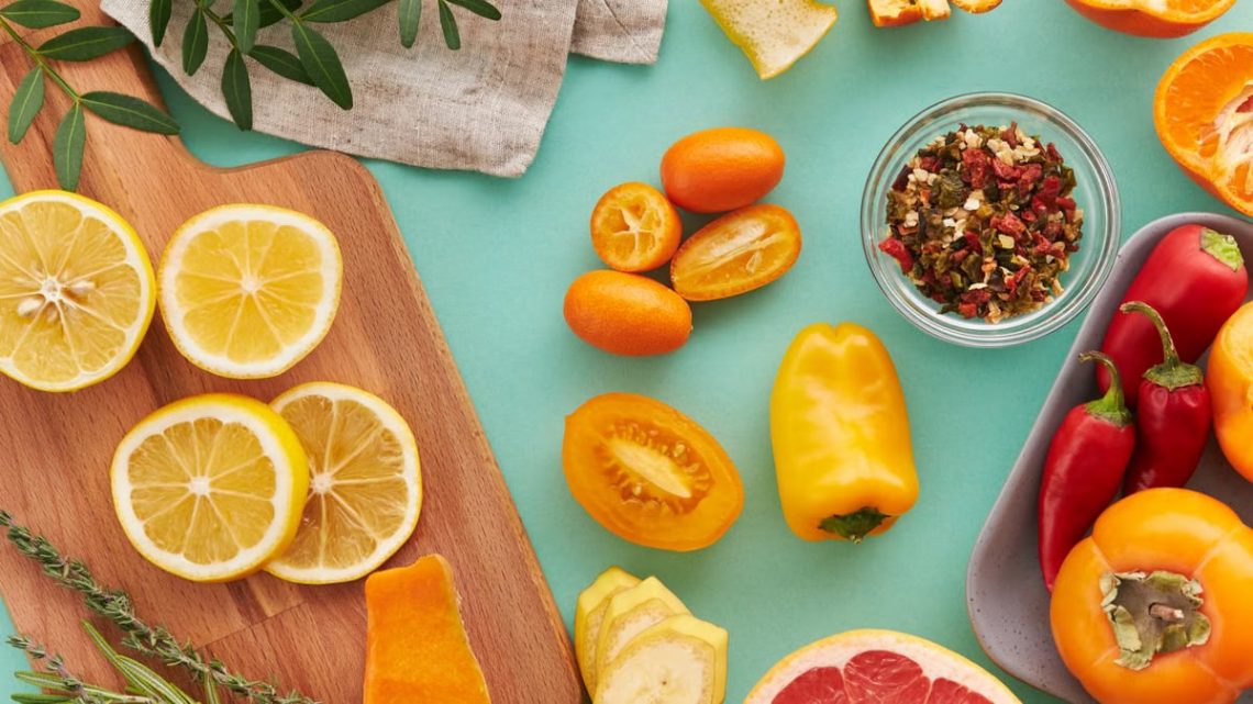 Colorful assortment of sliced fruits and vegetables on teal background, showcasing freshness.
